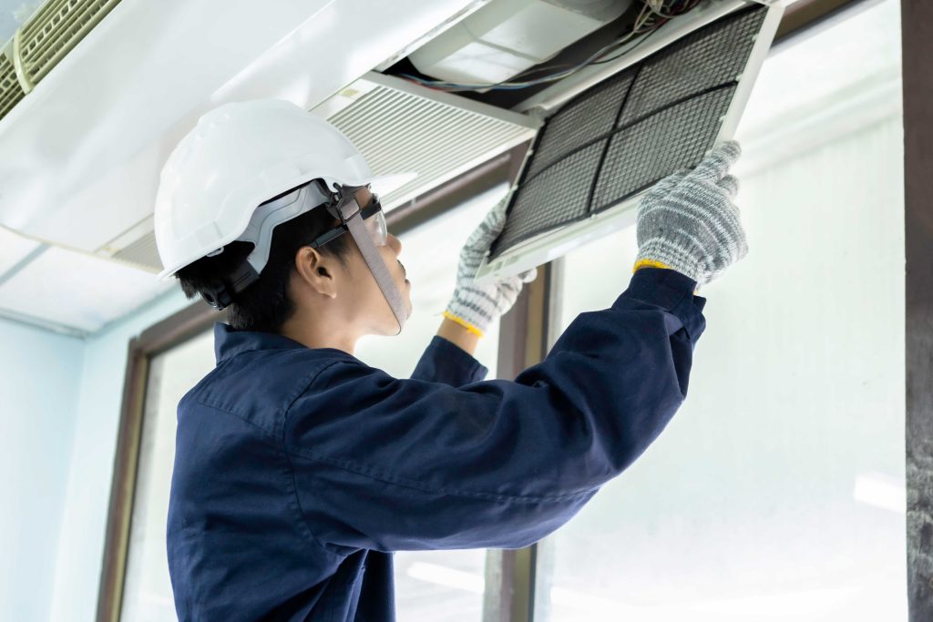 Técnico con casco y guantes revisando el filtro de un sistema de aire acondicionado en el techo. JyJ servicios integrales calama 