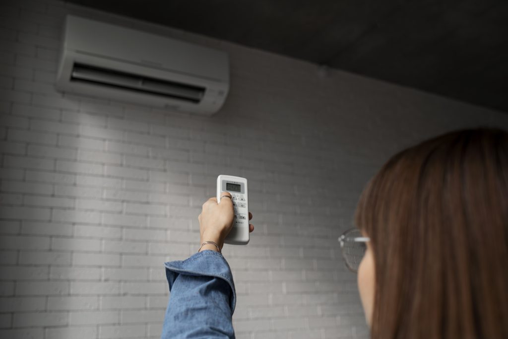 Persona ajustando la temperatura de un aire acondicionado con un control remoto en un interior con pared de ladrillo blanco